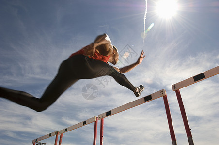 男性运动员在天空上跳跃障碍物的低角度视角男子奉献运动服双腿赛跑者轨道跨栏田径太阳专注背景图片