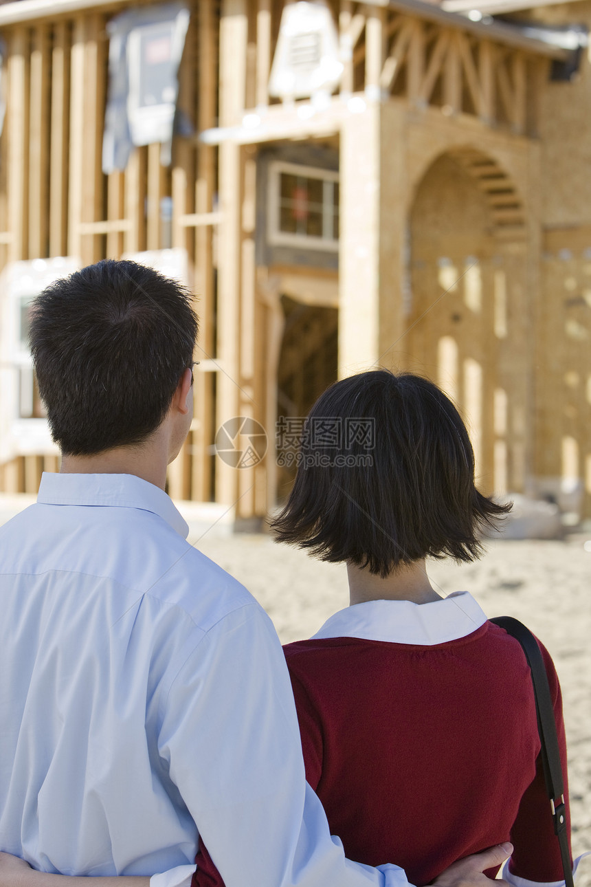 审视未完成的住房结构的成熟夫妇肩并肩站立的近视观图片