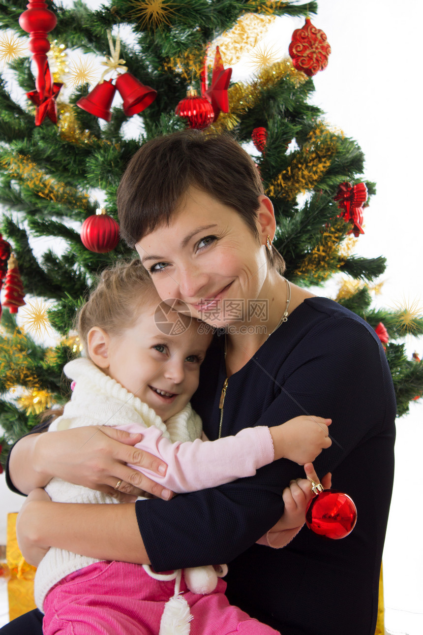 母亲在圣诞树下拥抱着女儿的母亲婴儿女士女性礼物孩子享受女孩帽子乐趣家庭图片