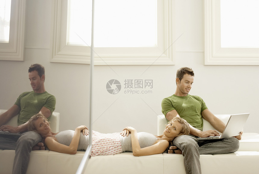 青年男子使用笔记本电脑 妇女躺在家中大腿上图片