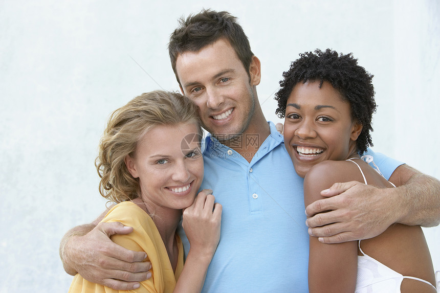 微笑的年轻男人的肖像 用双臂围着两个女性朋友靠墙图片