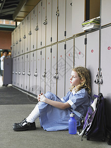 坐在地板上与学校储物柜对面的小学女孩的侧视角走廊高清图片素材