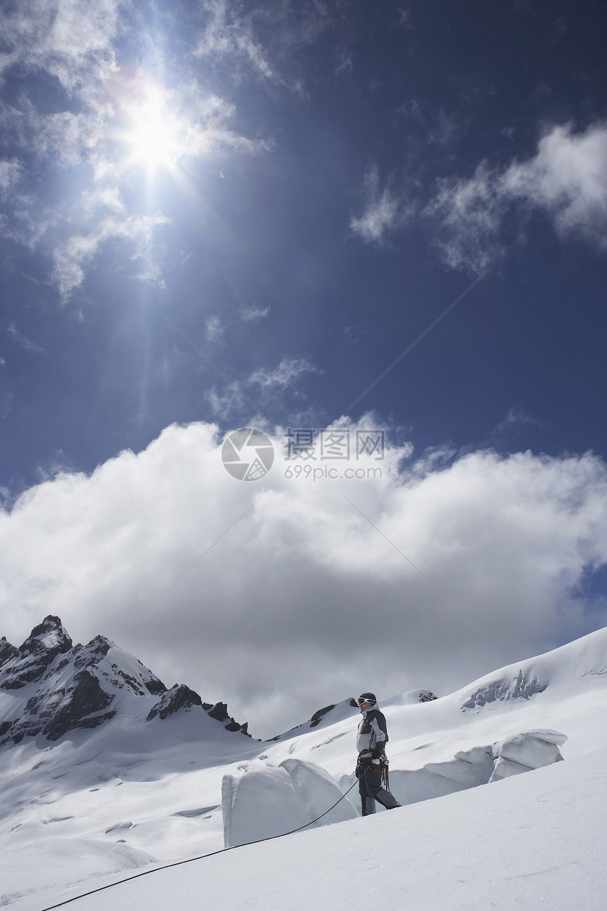 山上登山者站在雪坡对云和太阳的侧面图片