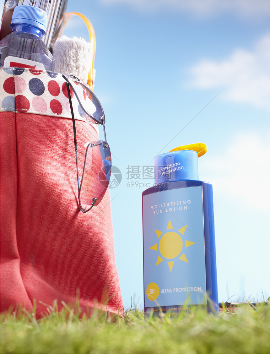 一瓶防晒霜和包袋 在草地上贴近沙滩图片