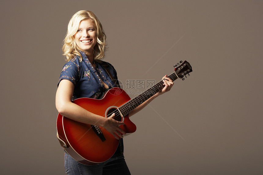快乐的年轻女子在棕色背景下弹吉他成人艺术家音乐家女士乡村吉他手音乐乐器工作室享受图片