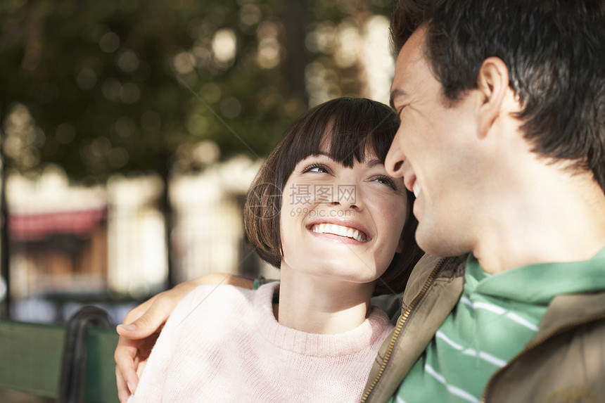 一对年轻夫妇在公园长椅上微笑着的一对小情侣图片