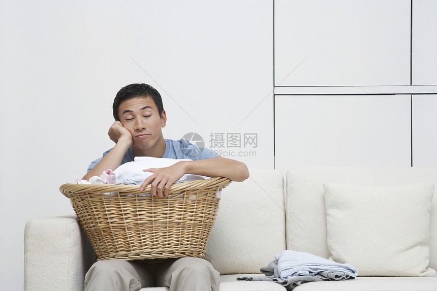 疲累的男人在索法的全衣洗衣篮上手头靠着头躺着图片