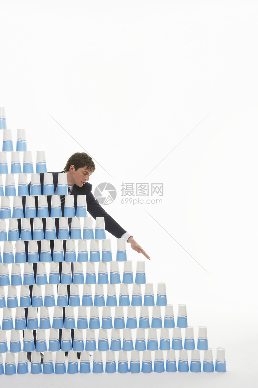 年轻商务人士在白色背景下把塑料杯堆成金字塔的青年商务人士图片