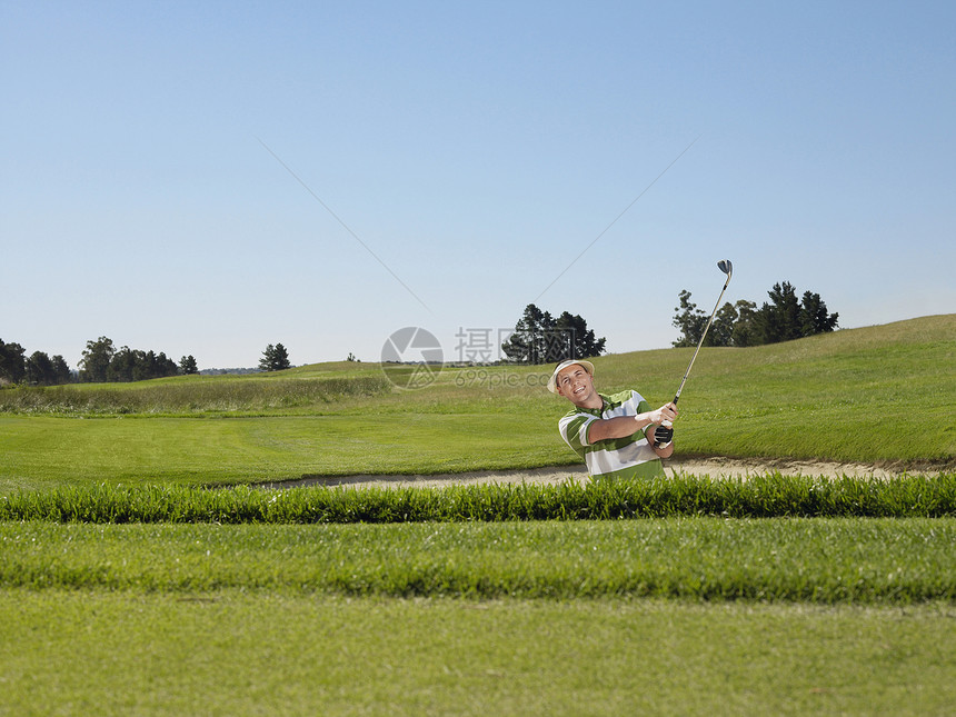 年轻男性高尔夫球手在沙陷中摇摆图片