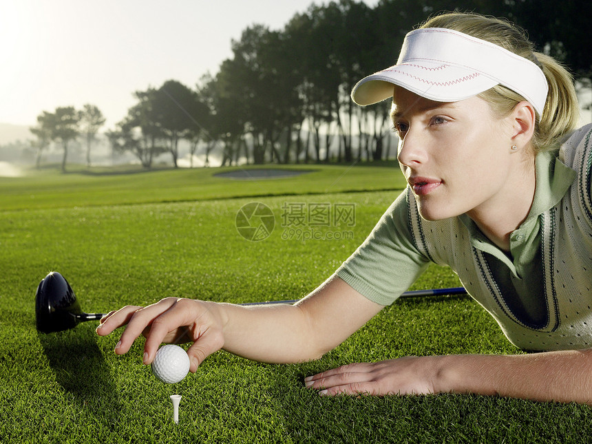 美丽的年轻女子高尔夫运动员躺在草地上 同时在踢球场上打球图片