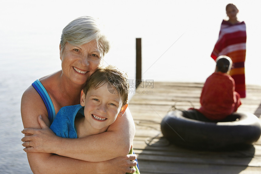 和背景姐妹在码头上拥抱孙孙孙子的快乐高龄妇女肖像图片