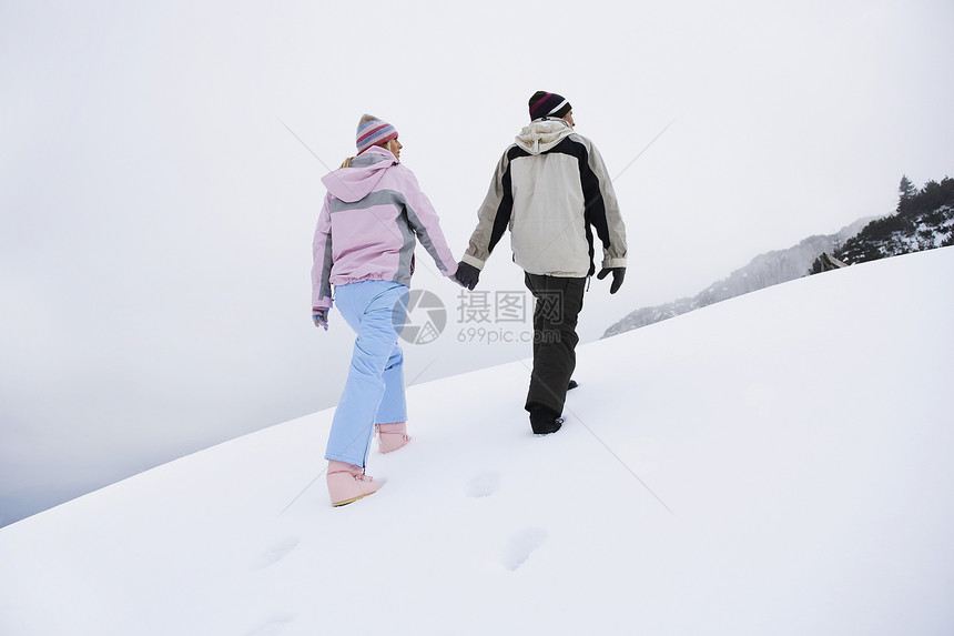 一对在雪覆盖的山丘上行走的夫妇 后仰低角视图丘陵女性女士中年人团结男人中年男子成人服装图片