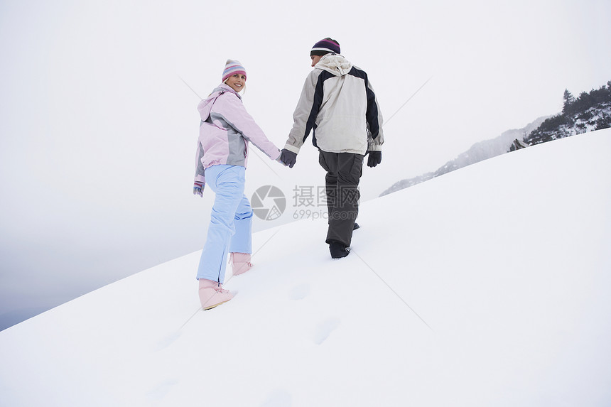 一对在雪覆盖的山丘上行走的夫妇 后仰低角视图成人服装眼神女士夫妻休闲两个人男子团结中年图片