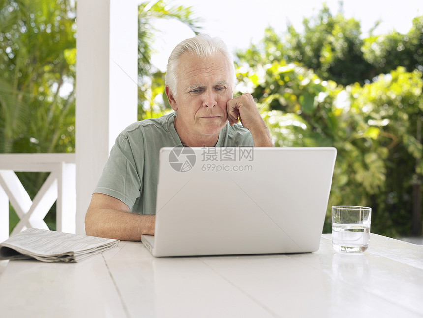 在verandah桌使用笔记本电脑的成熟男子玻璃技术椅子阳台头发退休桌子闲暇成人树木图片