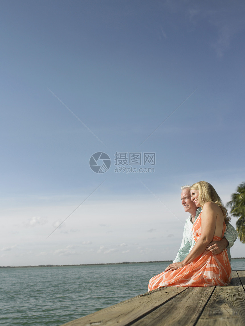 一对中年夫妇坐在码头边缘的侧面视图甲板退休闲暇亲热夫妻裙子团结异性天空男人图片