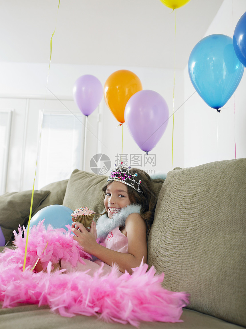 一个坐在沙发上 带着气球和纸杯蛋糕的快乐少女的肖像图片