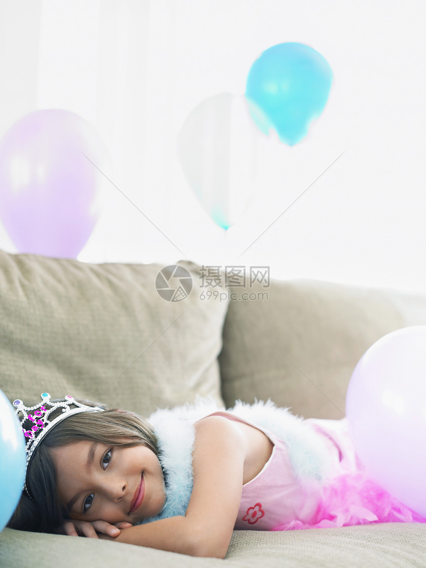 一个微笑的年轻女孩的肖像 躺在沙发上 带着气球派对孩子房间女性说谎蟒蛇长椅享受庆典皇冠图片