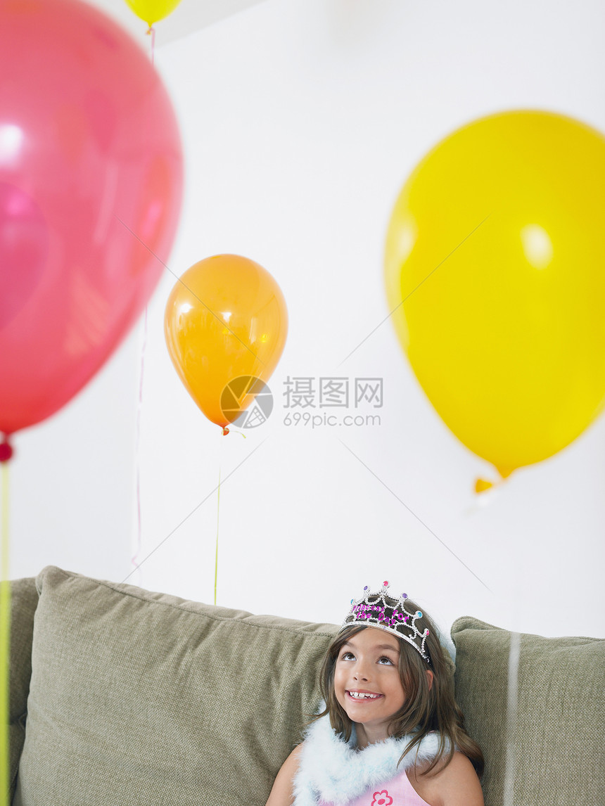 坐在沙发上看着气球的快乐女孩们沉思享受皇冠生日幸福女孩闲暇派对庆典长椅图片
