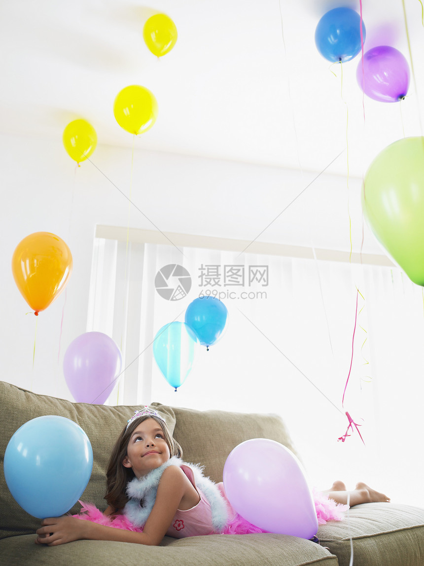年轻微笑的女孩躺在沙发上 仰着气球童年派对房间房子享受长椅蟒蛇孩子庆典说谎图片