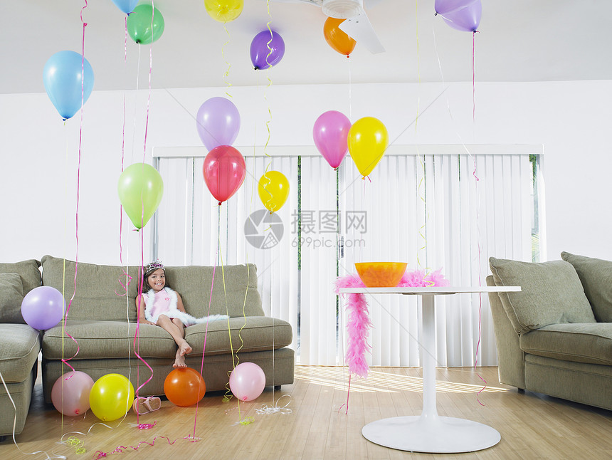 一个女孩坐在客厅里坐满气球的全身年轻女孩沉思孩子长椅闲暇庆典桌子童年裙子沙发派对图片