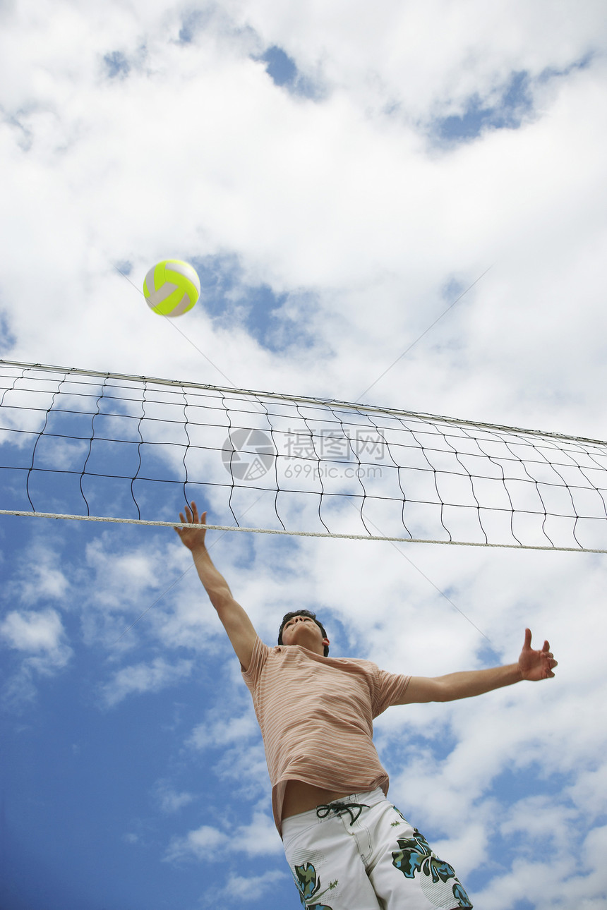 青少年男孩在沙滩排球对抗云天的低角度视角图片