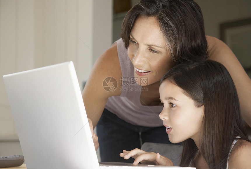 幸福母亲协助女儿在家使用笔记本电脑图片