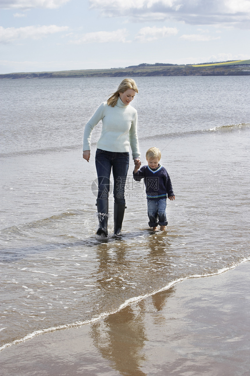 整个母亲和儿子在海滩上散步时手牵手图片