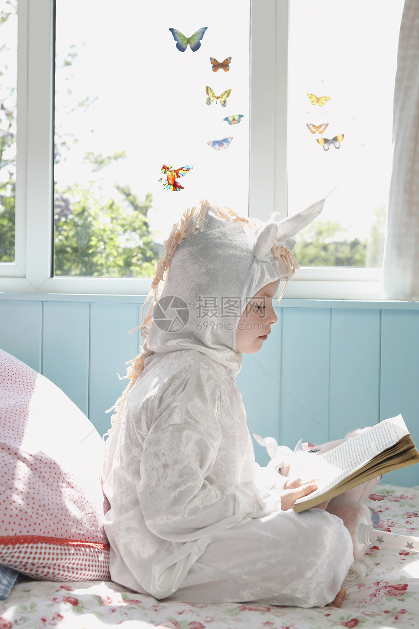 一个年轻女孩在床上 穿着独角兽服装看书的侧边景图片