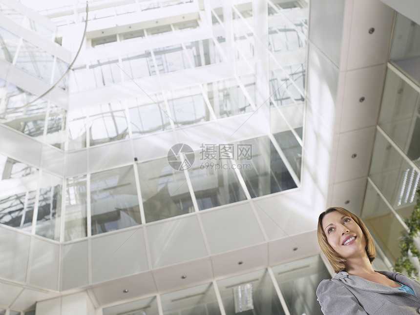 站在办公大楼阁楼的笑容女商务人士的低角度视角视图图片