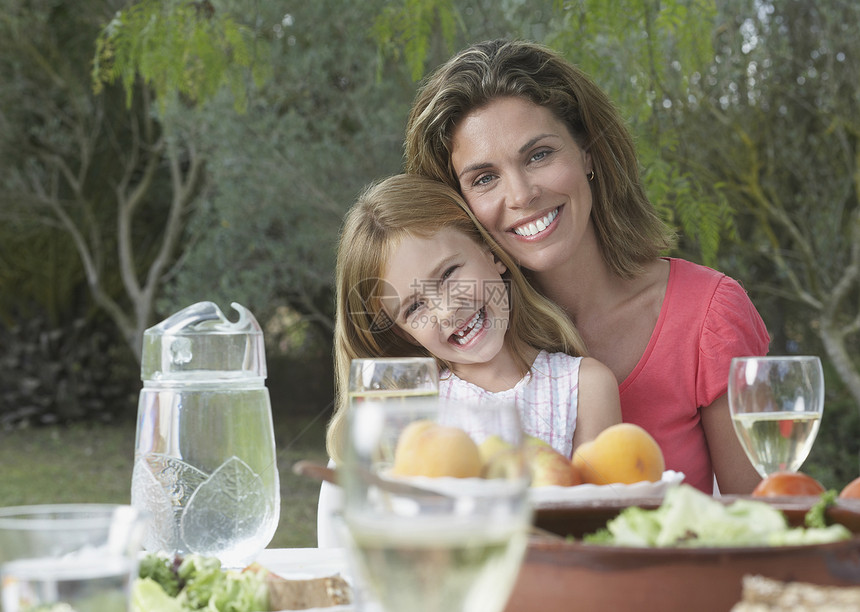 微笑的母亲和女儿坐在花园餐厅餐桌旁的肖像图片
