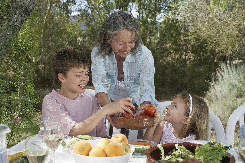 高级妇女在花园桌前送水果给微笑的孩子们吃图片
