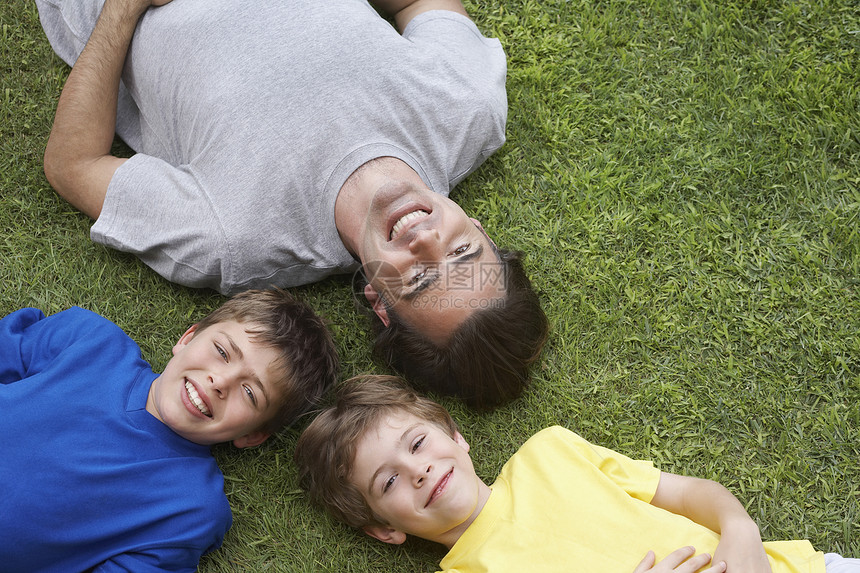 微笑的父亲和躺在草地上的两个儿子的更高视角图片