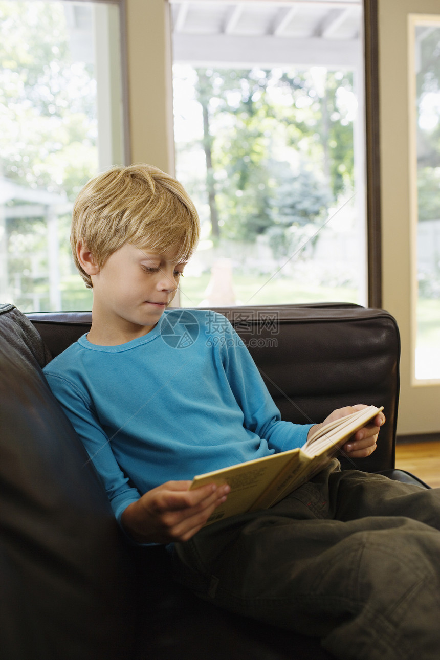 舒适的男孩坐在沙发上 在客厅用书看书图片