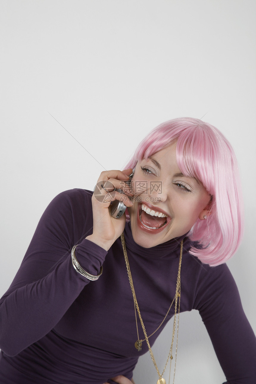 穿着粉红色假假发的年轻女子在移动电话中大笑图片