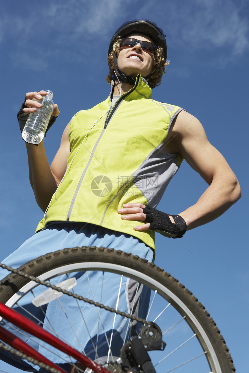 一位年轻男性骑自行车的男子在天空上举着一瓶水的低角度视角图片