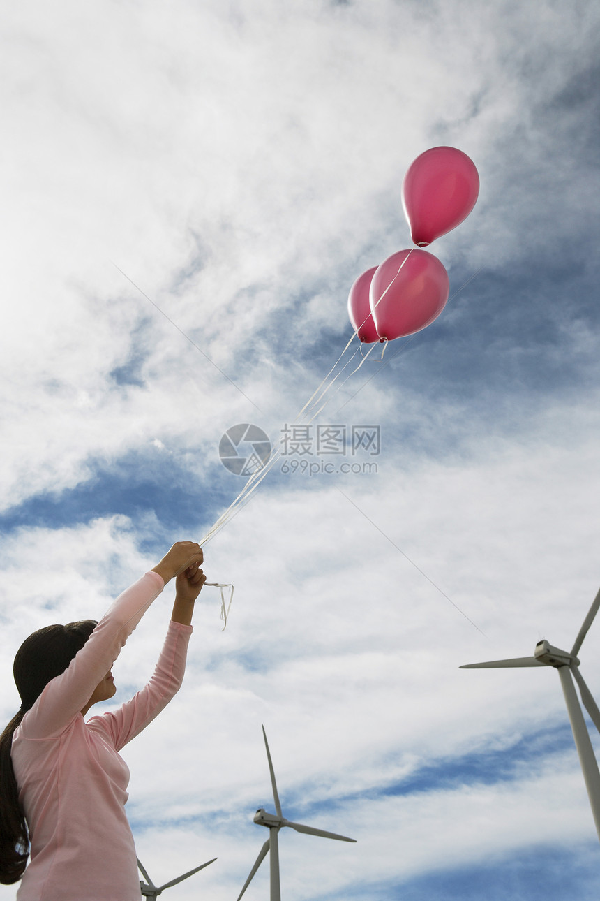 年轻女孩在风力农场玩粉红气球对抗云天图片