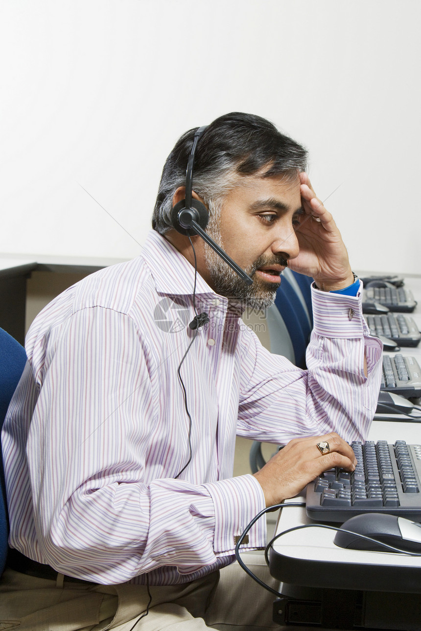 疲劳的客户服务运营商在键盘打字时用耳耳机进行沟通的侧面视图图片