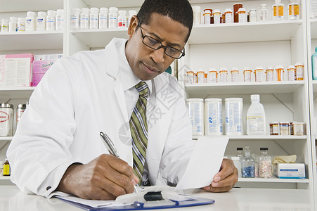 非裔美籍男药剂师在药店工作处方水平工作服货架专注男人补给品经销商药品架子白色的高清图片素材