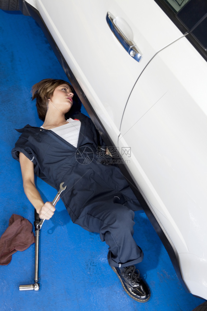 妇女躺在地板上 在汽车车库里做汽车工作图片