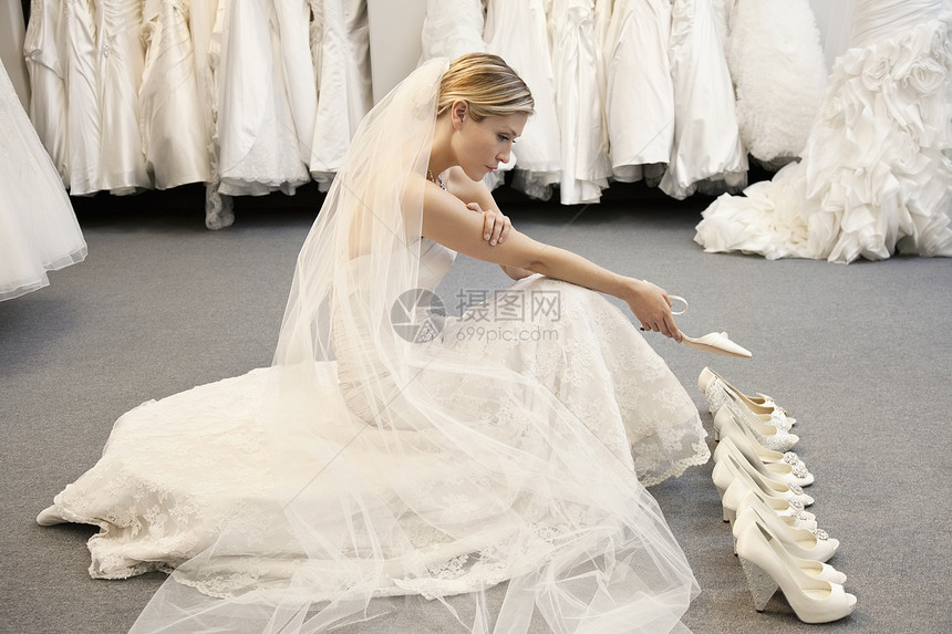 穿着婚纱的年轻女性的侧面观点在挑选鞋时混淆不清图片