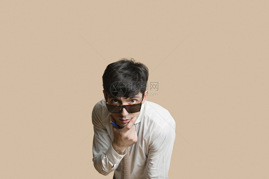 一名身戴墨镜的年轻男子的肖像 他的下巴用手遮着彩色背景图片