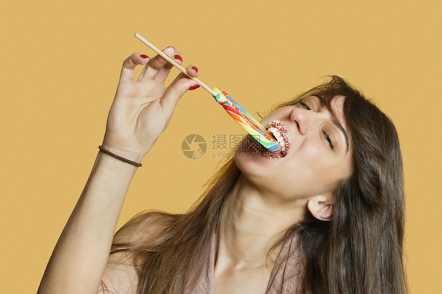 一位年轻女子在彩色背景上吃棒棒棒糖的肖像图片