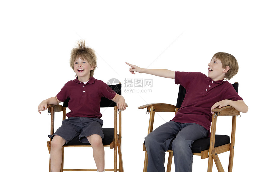 白色背景下坐在导演椅上的青春期前男孩指着朋友的头发图片
