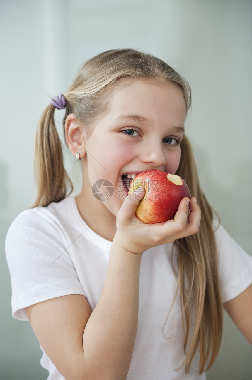 快乐的年轻女孩在灰色背景上吃苹果的肖像图片