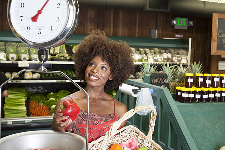 爆炸特价素材非裔美国妇女在超市按比例称量胡椒的非洲女性成人微笑卷发杂货种族短发成年展示闲暇棕榈背景