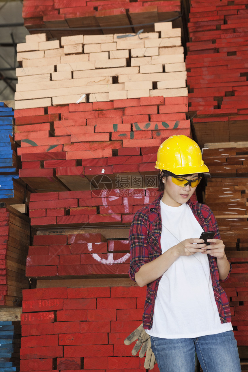 亚洲女性工业工人使用手机 背着堆叠的木木木板底部的移动电话图片