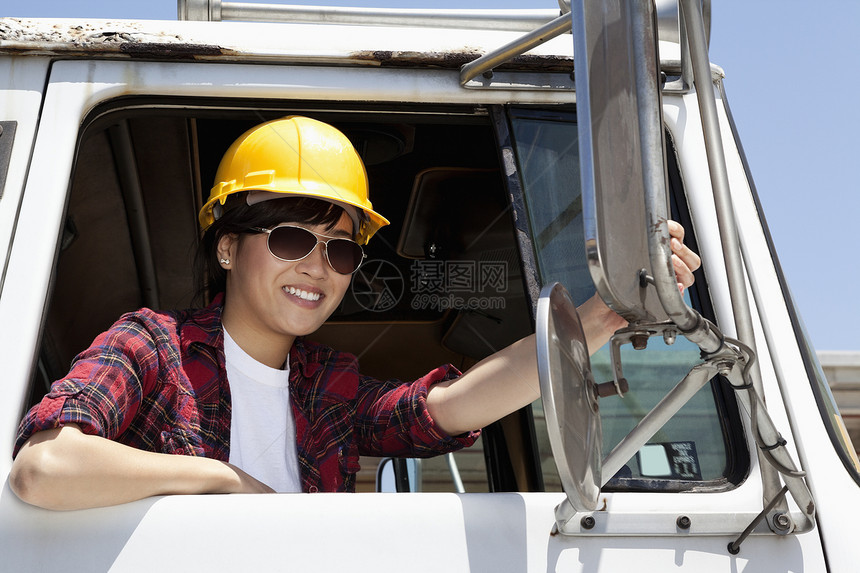 女工业工人在坐在伐木卡车上时调整镜镜的身影平板车车门陆地司机商业露齿安全帽驾驶座货车天空图片