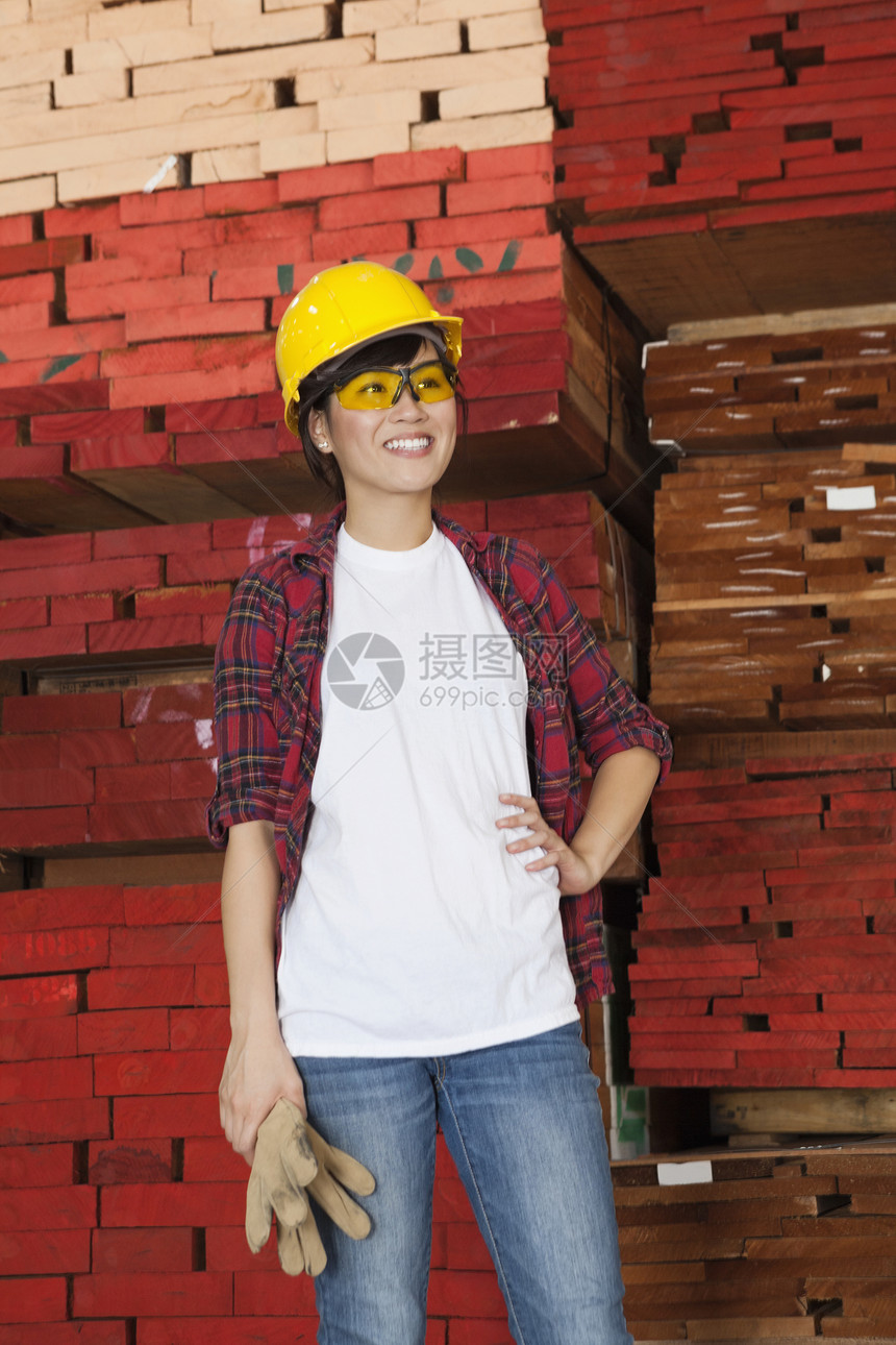 亚洲女性工业工人背着堆叠的木木板在背景中四处寻找图片