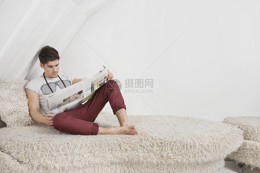 年轻男子坐在草沙发上看报纸时图片