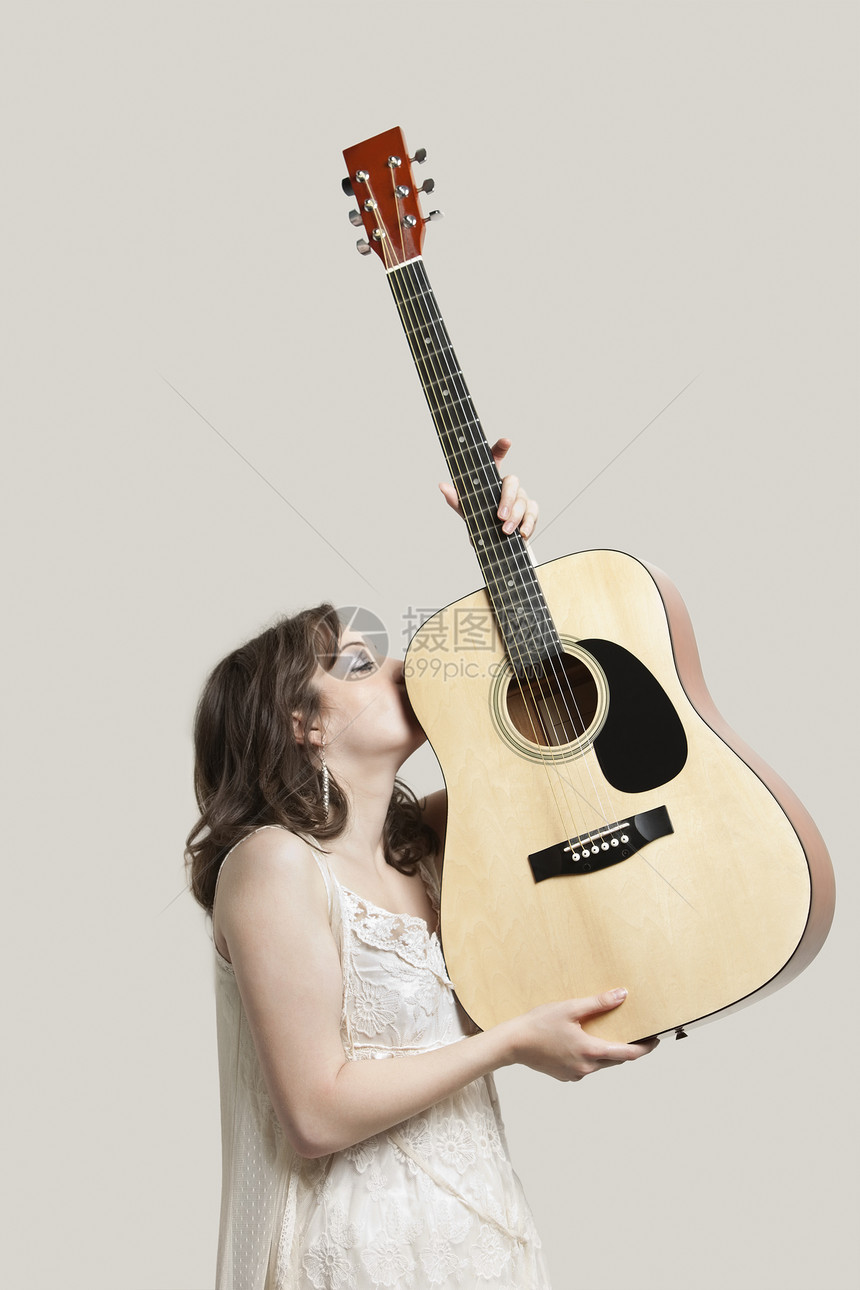 年轻女子在灰色背景下亲吻吉他图片